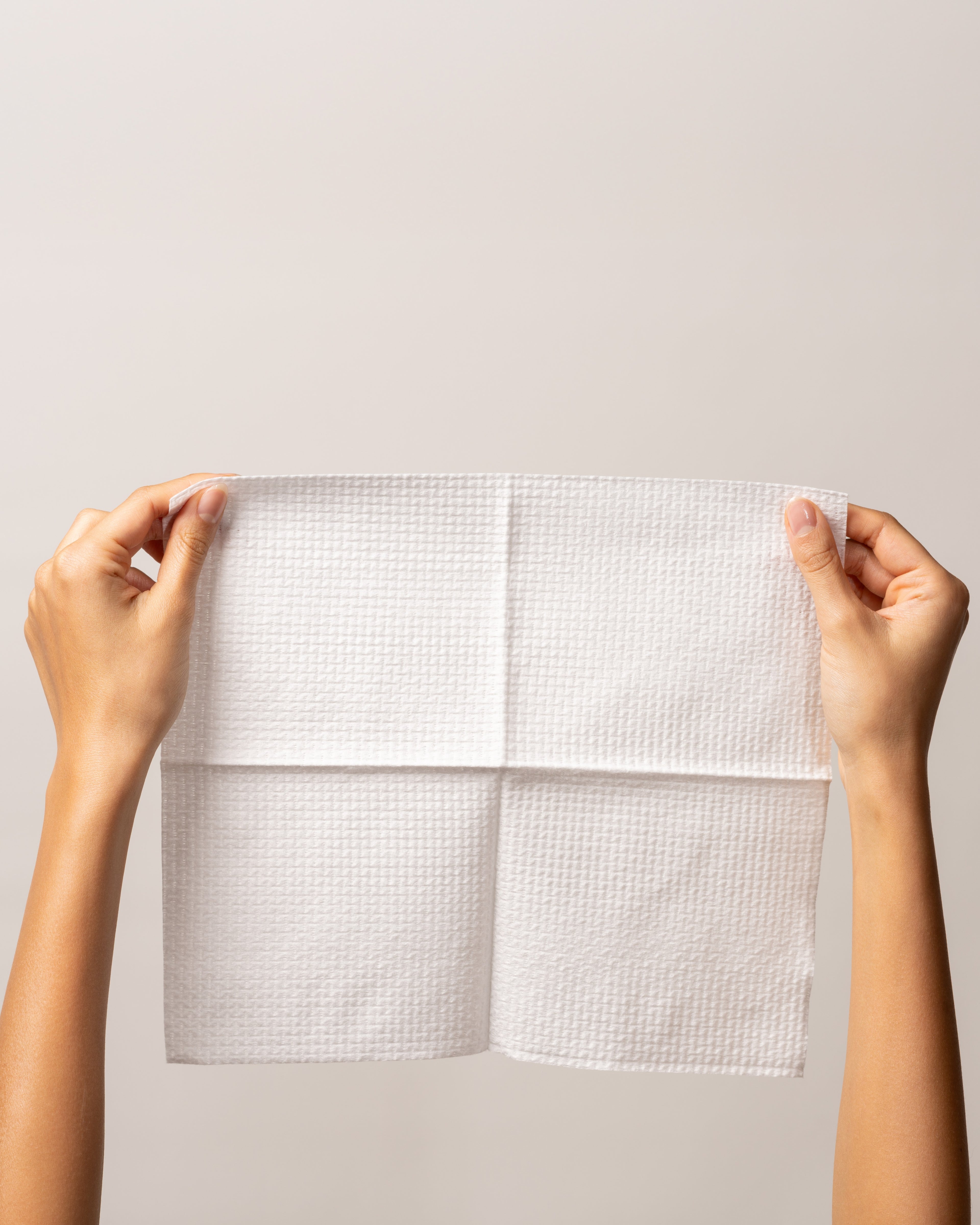 Hands holding a soft, white single-use towel from the Face Bundle for hygienic skincare.